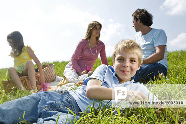 Boy lying in meadow  family in background