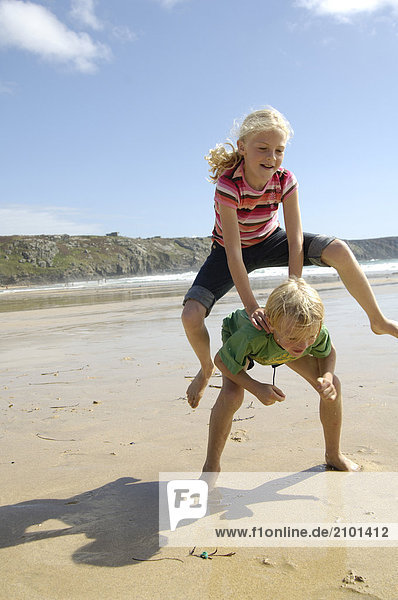 Zwei Kinder tun LeapFrosch am Strand