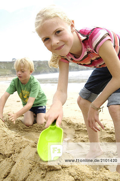 Porträt von Mädchen hält Schaufel mit ihrer Freundin machen Sandburg am Strand