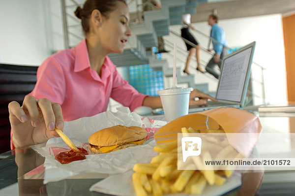 Geschäftsfrau isst Pommes frites  arbeitet am Laptop