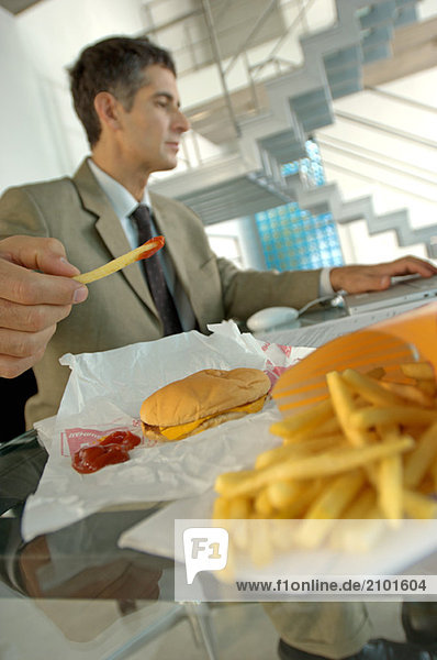 Mittlerer Erwachsener Geschäftsmann mit Burger und Pommes frites  mit Laptop