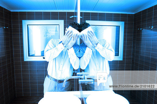 Mann  der das Gesicht bedeckt  während er sich im Waschraum an den Spiegel lehnt