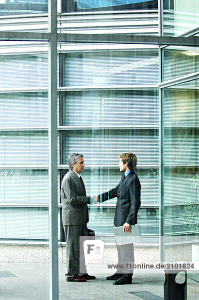 Businessmen shaking hands by office building