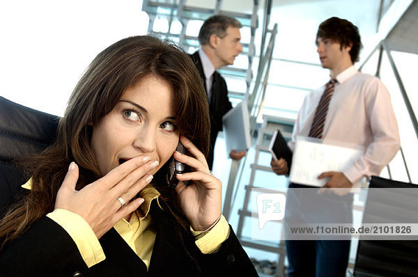 Businesswoman using mobile phone in office with colleagues in background