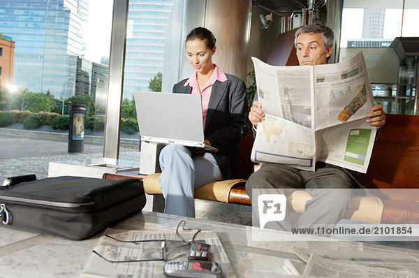 Businesswoman using laptop while businessman reading newspaper