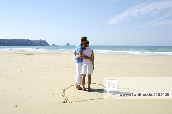 Rear view of couple standing in heartshape on beach