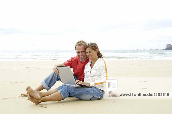 Close-up of couple using laptop on beach