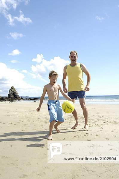 Father playing soccer with his son on beach