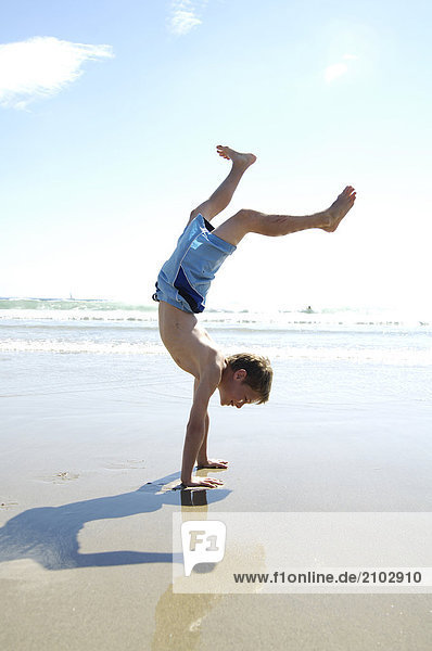 Side profile of boy doing handstand on beach