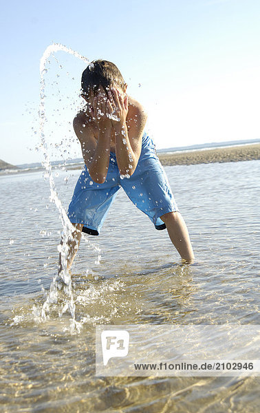 Boy washing his face on beach
