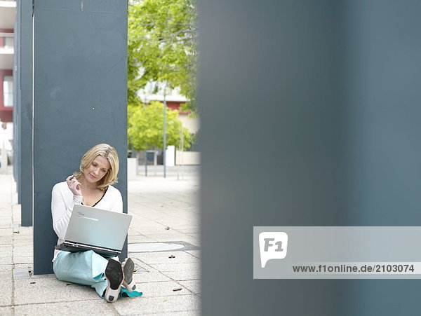 Geschäftsfrau am Straßenrand sitzen und mit laptop
