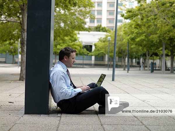 Seitenansicht Kaufmann am Straßenrand sitzen und mit laptop