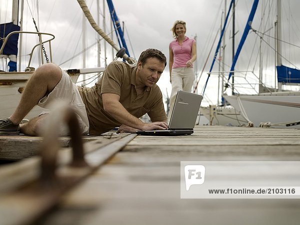 Mann mit Laptop im Hafen mit Frau im Hintergrund