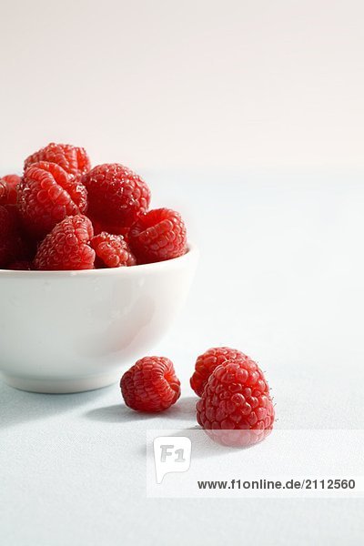 3 raspberries sit beside bowl of raspberries