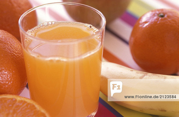 Glas frischer Orangensaft mit Früchten im Hintergrund