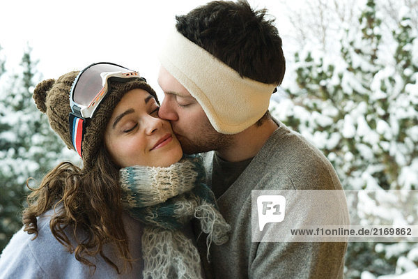 Young couple in winter clothing  man kissing woman on cheek