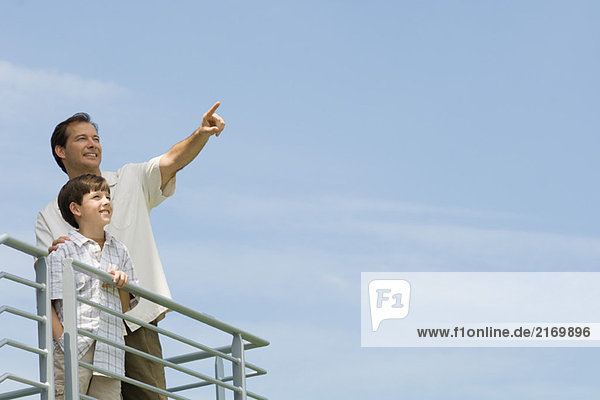 Man standing on balcony with son and pointing at sky
