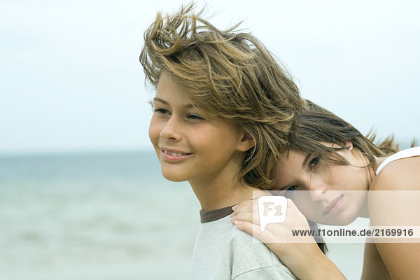 Teenagermädchen lehnt ihren Kopf gegen den jüngeren Bruder im Freien  schaut in die Kamera  Porträt