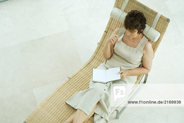 Frau sitzt auf einem Sessel und schreibt in einem Tagebuch.