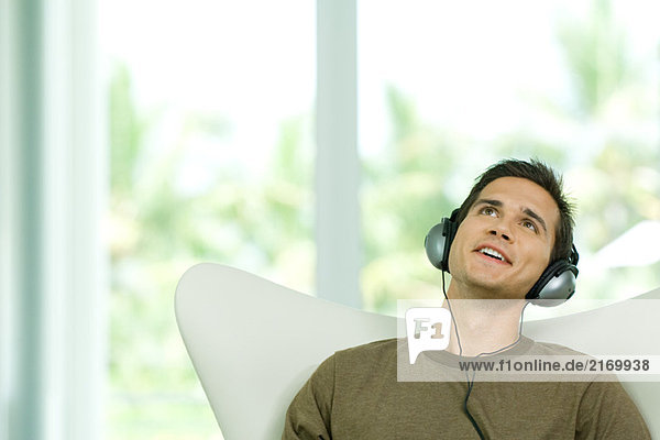 Young man listening to head phones  looking up  smiling