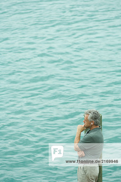 Mann steht neben dem Wasser und hört Kopfhörer  schaut weg  Blick in den hohen Winkel