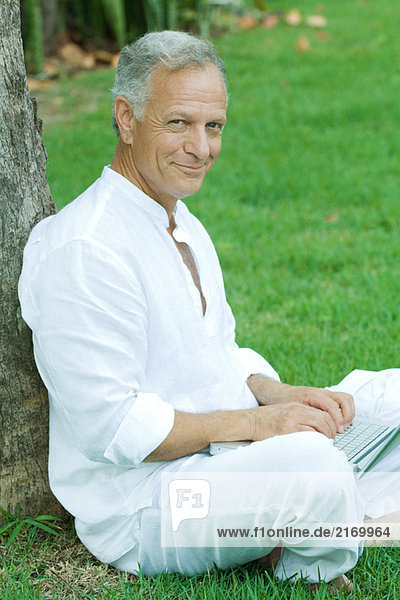 Mature man sitting outdoors using laptop computer  smiling at camera