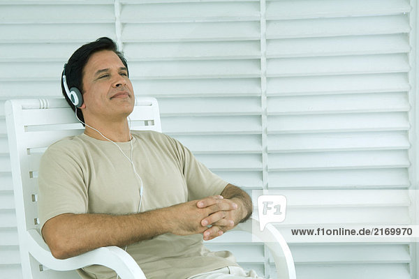 Mann sitzt im Stuhl und hört Kopfhörer  Augen halb geöffnet