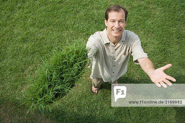 Man standing and holding clump of grass in one hand  smiling at camera  high angle view