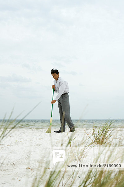Mann steht am Strand und fegt Sand mit Besen