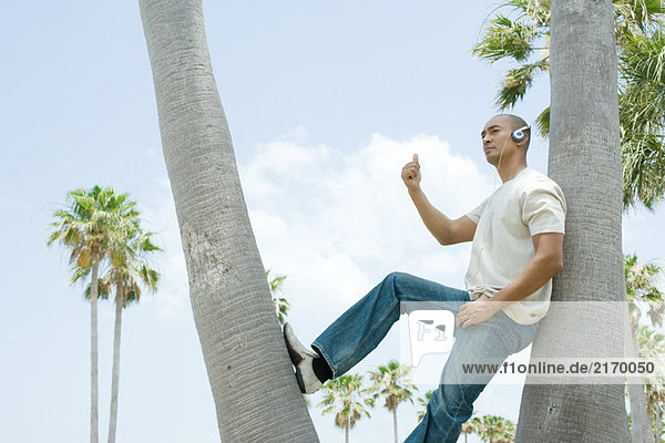 Man wearing headphones leaning against tree with thumb raised  looking away