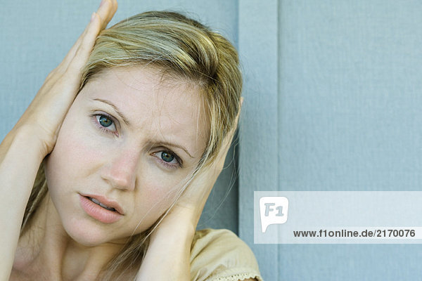 Woman covering ears with hands  frowning at camera