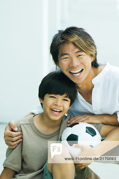 Junge hält Fußball und lächelt mit Vater in der Kamera  Porträt