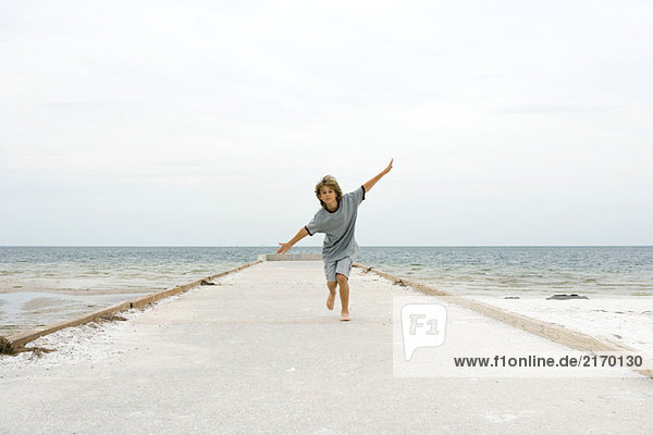 Boy running at the beach with arms outstretched  front view