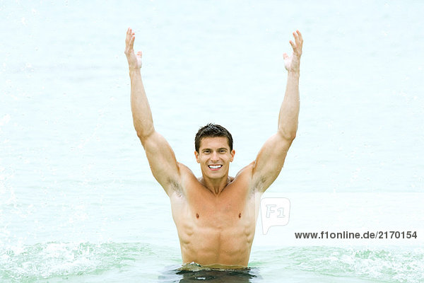 Muscular man standing in swimming pool with arms raised  smiling at camera