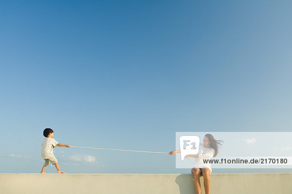 Junge und Frau spielen Tauziehen  blauer Himmel im Hintergrund