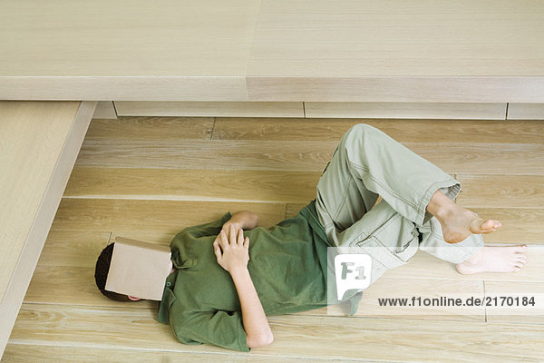 Junge auf dem Boden liegend mit Buch über dem Gesicht