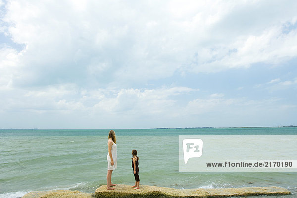 Mutter und Tochter am Meer stehend  Blick zum Horizont  volle Länge