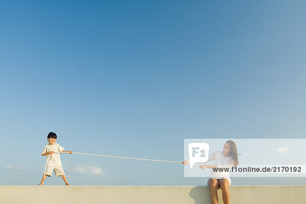 Kleiner Junge und Frau beim Tauziehen  blauer Himmel im Hintergrund