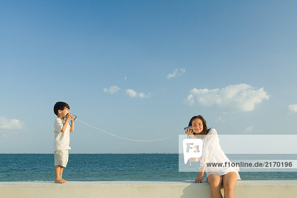 Junge spricht mit Frau durch Blechdose Telefon  Ozean Horizont im Hintergrund