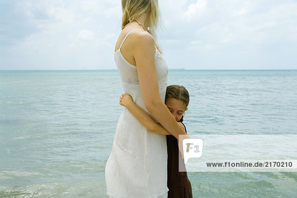 Mutter und Tochter stehen am Wasser  umarmend  Ozeanhorizont im Hintergrund