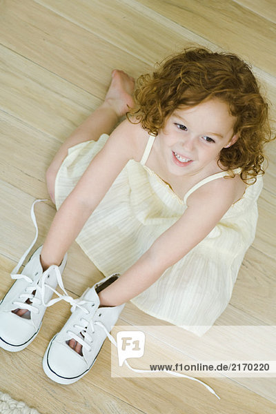 Kleines Mädchen auf dem Boden mit Händen in Schuhen  lächelnd  Blick von oben
