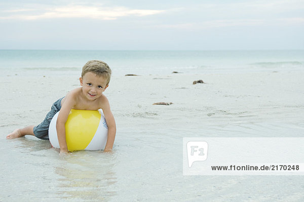 Kleiner Junge auf Strandball liegend  lächelnd vor der Kamera  volle Länge