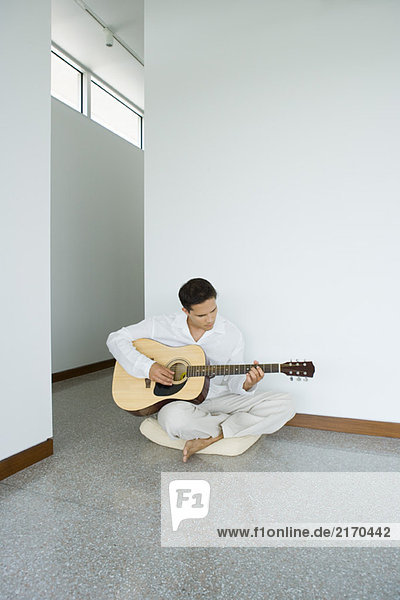 Man sitting on cushion playing acoustic guitar