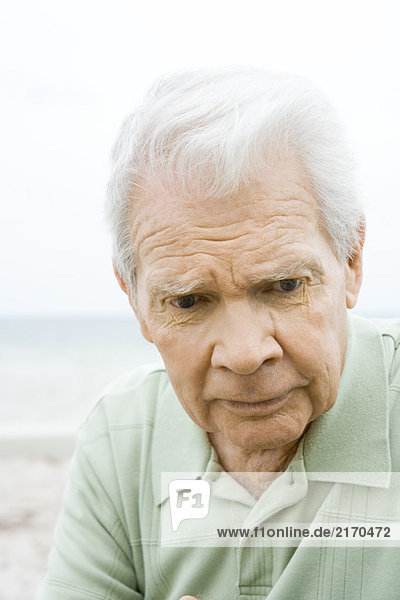 Senior man looking down  furrowing brow  close-up
