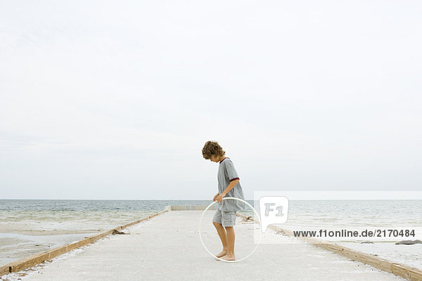 Junge auf dem Pier stehend mit Kunststoffreifen  Blick nach unten  Seitenansicht