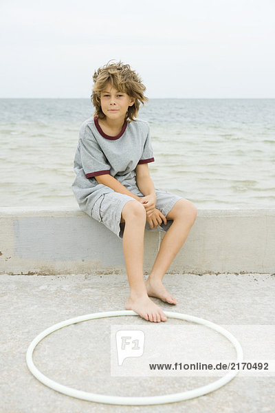 Junge sitzt auf einer niedrigen Wand am Strand  Fuß berührt Plastikband