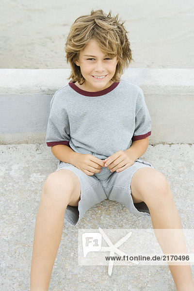 Junge sitzt auf dem Boden neben dem Seestern und lächelt vor der Kamera.
