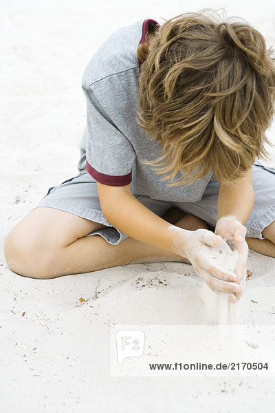 Junge sitzt auf dem Boden und spielt im Sand.