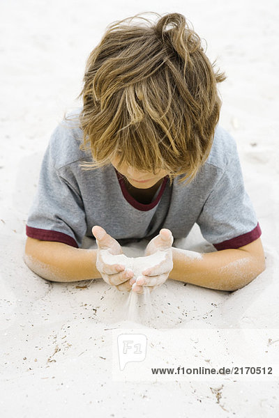 Junge liegt auf dem Boden und schaut auf eine Handvoll Sand.