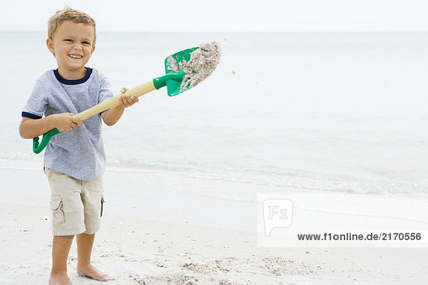 Young boy holding up shovel and throwing sand  smiling at camera